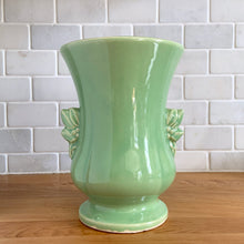Load image into Gallery viewer, Beautiful vintage Art Deco pale green handled trumpet vase #282 features berry and leaf handles. Crafted by McCoy Pottery, 1946. This vase is must for any art pottery collector. A lovely way to enhance your home&#39;s decor or to give as a gift!

In great vintage condition, chip to underside of foot, no cracks/repairs. Typical manufacturer&#39;s glaze pops/defects. Maker&#39;s mark on the bottom.

Measures 6 x 8 1/8 inches (incl. handle/spout)
