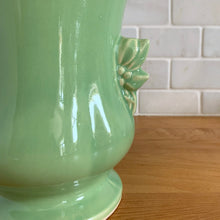 Load image into Gallery viewer, Beautiful vintage Art Deco pale green handled trumpet vase #282 features berry and leaf handles. Crafted by McCoy Pottery, 1946. This vase is must for any art pottery collector. A lovely way to enhance your home&#39;s decor or to give as a gift!

In great vintage condition, chip to underside of foot, no cracks/repairs. Typical manufacturer&#39;s glaze pops/defects. Maker&#39;s mark on the bottom.

Measures 6 x 8 1/8 inches (incl. handle/spout)
