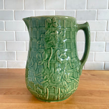 Load image into Gallery viewer, Vintage art deco gloss green ceramic yellow ware pitcher featuring climbing roses on a trellis pattern. Crafted by McCoy Pottery, USA, 1920s. A beautiful piece to add to your art pottery collection!

In excellent condition, no chips/cracks/repairs, age-related crazing. Typical manufacturing glaze pops. Unmarked.

Measures 5 1/4 x 8 3/4 inches

