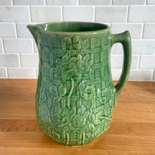 Load image into Gallery viewer, Vintage art deco gloss green ceramic yellow ware pitcher featuring climbing roses on a trellis pattern. Crafted by McCoy Pottery, USA, 1920s. A beautiful piece to add to your art pottery collection!

In excellent condition, no chips/cracks/repairs, age-related crazing. Typical manufacturing glaze pops. Unmarked.

Measures 5 1/4 x 8 3/4 inches
