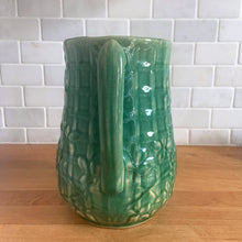 Load image into Gallery viewer, Vintage art deco gloss green ceramic yellow ware pitcher featuring climbing roses on a trellis pattern. Crafted by McCoy Pottery, USA, 1920s. A beautiful piece to add to your art pottery collection!

In excellent condition, no chips/cracks/repairs, age-related crazing. Typical manufacturing glaze pops. Unmarked.

Measures 5 1/4 x 8 3/4 inches
