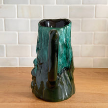 Load image into Gallery viewer, Vintage green drip glaze pitcher, featuring a woodland design of raised mushrooms and knots around a tree trunk. Crafted by Evangeline Pottery, Canada, 1960s. This sweet pitcher makes for a beautiful statement piece or a functional pitcher for your home.

In excellent condition, no chips/cracks/repairs.

Measures 5 x 3 5/8 x 6 1/4 inches
