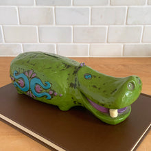 Load image into Gallery viewer, Adorable vintage happy green hippopotamus coin bank. This smiling hippo has white teeth, purple tongue and is embossed with a colourful fun on either side in blue and purple. Crafted by Pride Creations Inc. USA and made in Japan, 1970s. Makes a great retro decor piece for a nursery or child&#39;s bedroom or playroom!

In good vintage condition, no chips or cracks. No rubber stopper.

Measures 10 x 3 3/4 x 3 inches
