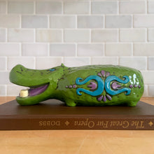 Load image into Gallery viewer, Adorable vintage happy green hippopotamus coin bank. This smiling hippo has white teeth, purple tongue and is embossed with a colourful fun on either side in blue and purple. Crafted by Pride Creations Inc. USA and made in Japan, 1970s. Makes a great retro decor piece for a nursery or child&#39;s bedroom or playroom!

In good vintage condition, no chips or cracks. No rubber stopper.

Measures 10 x 3 3/4 x 3 inches
