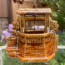 Load image into Gallery viewer, This classic vintage ochre and green ceramic planter features a charming figural wishing well design complete with a bucket and its original brass chain. Inscribed with the phrase &quot;Oh Wishing Well, Grant A Wish To Me,&quot; it adds a whimsical touch to any home decor. Crafted by McCoy Pottery, 1950s. Ideal for collectors of art pottery, this piece combines nostalgic appeal with functional beauty, making it a distinctive gift or a unique addition to your collection.
