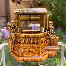 Load image into Gallery viewer, This classic vintage ochre and green ceramic planter features a charming figural wishing well design complete with a bucket and its original brass chain. Inscribed with the phrase &quot;Oh Wishing Well, Grant A Wish To Me,&quot; it adds a whimsical touch to any home decor. Crafted by McCoy Pottery, 1950s. Ideal for collectors of art pottery, this piece combines nostalgic appeal with functional beauty, making it a distinctive gift or a unique addition to your collection.
