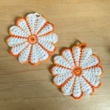 Load image into Gallery viewer, Unique and timeless, this pair of vintage hand crochet trivets are the perfect addition to any kitchen. Featuring a beautiful white and orange flower design, they are sure to bring a charming touch to your tablescape. Each trivet comes with its own hanger, making it easy to display and store...decor and function all in one!  Both are in excellent condition.  Each measures 5 1/2 inches
