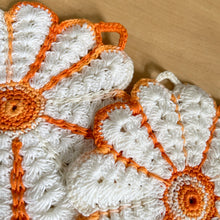 Load image into Gallery viewer, Unique and timeless, this pair of vintage hand crochet trivets are the perfect addition to any kitchen. Featuring a beautiful white and orange flower design, they are sure to bring a charming touch to your tablescape. Each trivet comes with its own hanger, making it easy to display and store...decor and function all in one!  Both are in excellent condition.  Each measures 5 1/2 inches
