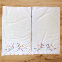 Load image into Gallery viewer, A lovely pair of vintage white cotton pillowcases, featuring hand embroidered pink, blue flowers with green leaves, a path of turquoise and two golden butterflies, plus a finished scalloped edge in pink. A gorgeous addition to your bed linens! In good vintage condition. Measures 31 x 18 1/2 inches
