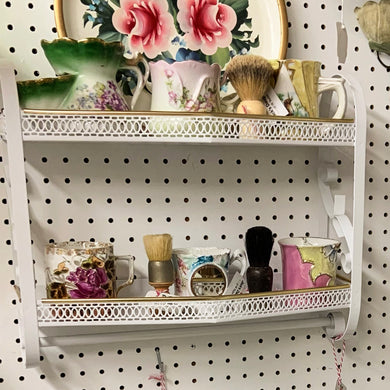 Vintage Hollywood Regency style wall hung 2-tier metal shelf painted white and trimmed with gold edging plus a towel bar. A great piece for storing bits and pieces in the bath or mudroom. Circa 1950s/60s.  In excellent condition, freshly painted with rust inhibitor paint.