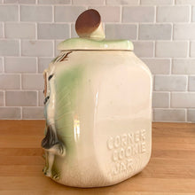 Load image into Gallery viewer, This rare vintage ceramic corner cookie jar features brunette and blonde cheerleaders in old-fashioned outfits, cheering underneath the words Have A Cookie in between is a megaphone on the grass that reads cookie time all glazed in shades of green, blue, yellow brown and black on a cream ground, topped with a rust-brown megaphone on the lid. The piece-de-resistance are the cheerleaders holographic facial expressions that change from eyes open with a wide smile to eyes shut with closed smiles. 
