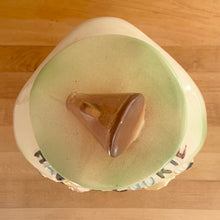 Load image into Gallery viewer, This rare vintage ceramic corner cookie jar features brunette and blonde cheerleaders in old-fashioned outfits, cheering underneath the words Have A Cookie in between is a megaphone on the grass that reads cookie time all glazed in shades of green, blue, yellow brown and black on a cream ground, topped with a rust-brown megaphone on the lid. The piece-de-resistance are the cheerleaders holographic facial expressions that change from eyes open with a wide smile to eyes shut with closed smiles. 
