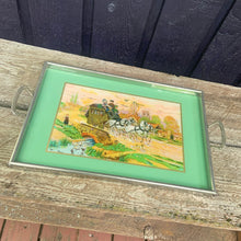 Load image into Gallery viewer, Stunning vintage reverse painted foil art pewter framed handled tray featuring a country landscape, with gold carriage coach, white horses and passengers. The handles show Rene Macintosh style rosettes. Crafted by Rusch, Germany, 1920s. Perfect as a vanity tray, to serves drinks and snacks or even wall art.

The painting is in excellent condition with minor age-related wear.

Measures 17 3/8 x 11 1/2 (19 5/8 with handles)
