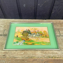 Load image into Gallery viewer, Stunning vintage reverse painted foil art pewter framed handled tray featuring a country landscape, with gold carriage coach, white horses and passengers. The handles show Rene Macintosh style rosettes. Crafted by Rusch, Germany, 1920s. Perfect as a vanity tray, to serves drinks and snacks or even wall art.

The painting is in excellent condition with minor age-related wear.

Measures 17 3/8 x 11 1/2 (19 5/8 with handles)
