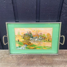 Load image into Gallery viewer, Stunning vintage reverse painted foil art pewter framed handled tray featuring a country landscape, with gold carriage coach, white horses and passengers. The handles show Rene Macintosh style rosettes. Crafted by Rusch, Germany, 1920s. Perfect as a vanity tray, to serves drinks and snacks or even wall art.

The painting is in excellent condition with minor age-related wear.

Measures 17 3/8 x 11 1/2 (19 5/8 with handles)
