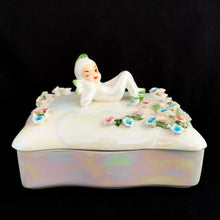 Load image into Gallery viewer, Iridescent white Lefton porcelain trinket box, front view showing reclining pixie figurine on lid with pink and blue applied flowers, lustrous pearl glaze on black background
