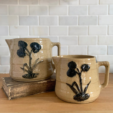 Vintage natural yellow ware strapped barrel milk pitcher featuring navy lily in bas relief with rope style handle, No. 21171. Crafted by Robinson Ransbottom Pottery Co., USA, 1930s. Enhance your home's decor with this beautiful piece of primitive farmhouse tableware. A wonderful addition to any art pottery collection!

Excellent vintage condition, no chips/cracks/repairs, age-related crazing and typical manufacturer's glaze pops. Unmarked

Option 1: 4 x 4 1/8 inches. 32 oz
Option 2: 5 1/4 x 5 1/4. 48 oz