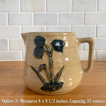 Load image into Gallery viewer, Vintage natural yellow ware strapped barrel milk pitcher featuring navy lily in bas relief with rope style handle, No. 21171. Crafted by Robinson Ransbottom Pottery Co., USA, 1930s.

Enhance your home's decor with this beautiful piece of primitive farmhouse tableware. A wonderful addition to any art pottery collection!

Option 3: Measures 4 x 4 1/2 inches. In excellent vintage condition, no chips/cracks/repairs with age-related crazing and typical manufacturer's glaze pops. Unmarked. Capacity 32 ounces
