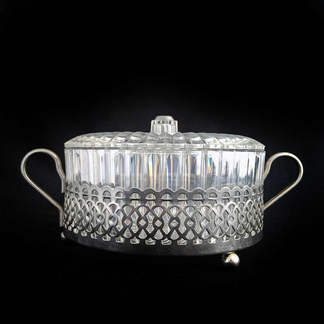 Clear faceted lucite plastic lidded vanity box nestled in a silver ormolu handled caddy. The silver-toned metal ormolu caddy has two handles and three ball feet. An excellent addition to your boudoir or bathroom vanity for powder or trinkets. In excellent vintage condition, free from chips. Measures 5 1/8 x 3 1/2 (not incl. handles)