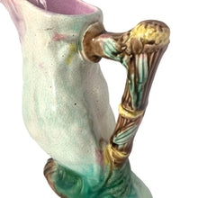 Load image into Gallery viewer, Antique majolica figural white and pink cockatoo parrot ceramic pitcher with green botanical base and brown bamboo-style handle. Crafted by Georges Jones, England, in the late 19th century (1880s). A wonderful piece of whimsical majolica for any collector and lends itself nicely to a tropical or Tiki themed decor!

In good used vintage condition, no chips. Age-related crazing and typical manufacturing glaze bubbles present. See photos.

Measures 5 x 2 1/2 x 6 inches
