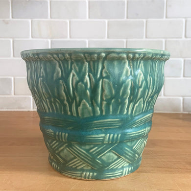 Vintage art deco matte teal ceramic jardiniere planter featuring repeating columns of stacked palm leaves atop a basket weave pattern. Crafted by Robinson Ransbottom Pottery Co., USA, 1930s. A beautiful piece to add to your art pottery collection!

In excellent condition, no chips/cracks/repairs. Typical manufacturing glaze pops. Marked 112/-.

Measures 7 x 5 1/2 inches