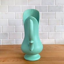 Load image into Gallery viewer, Rare vintage mid-century matte turquoise vase with decorative handle. Crafted by McCoy Pottery, 1950s. This vase is must for any art pottery collector! Makes a perfect mid-century decor statement or give as a gift.

In good condition, slim chip to the handle, no cracks/repairs. Maker&#39;s mark on the bottom.

Measures 6 x 9 inches (incl. handle/spout)
