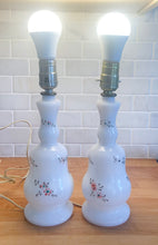 Load image into Gallery viewer, A beautifully shaped pair of vintage milk glass table lamps featuring hand painted flowers in orange, green and gold. Perfect for adding vintage charm to any space. In as found vintage condition, glass is free from chips/cracks, paint is worn. Tested and in working order. Measures 3 7/8 x 12 1/4 inches
