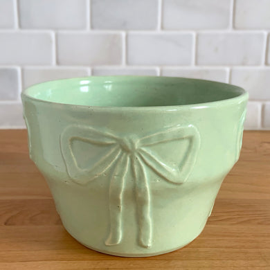 Vintage mint green embossed bows ceramic jardiniere planter, No. 287. Crafted by Robinson Ransbottom Pottery Co., 1940s. A beautiful piece to fill with your favourite houseplant and add to your art pottery collection!

In excellent vintage condition, no chips/cracks/repairs. Typical manufacturers glaze pops. Maker's mark.

Measures 6 x 4 inches