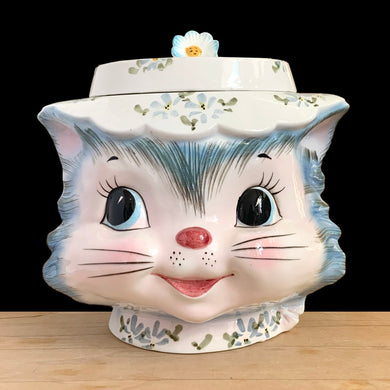 Adorable vintage hand painted Miss Priss anthropomorphic blue kitty cat head ceramic cookie jar. Lefton, Japan, 1950s. Highly sought after, this sweet cookie jar represents the epitome of collectible kitsch kitchen decor!

The vessel is in excellent condition, no chips/cracks/repairs. The lid has a repair to the top and several chips with one to the back of the flower, none detract from display or function, please see photos for details.

Measures 7 1/2 x 6 x 7 1/2 inches
