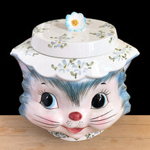 Load image into Gallery viewer, Adorable vintage hand painted Miss Priss anthropomorphic blue kitty cat head ceramic cookie jar. Lefton, Japan, 1950s. Highly sought after, this sweet cookie jar represents the epitome of collectible kitsch kitchen decor!

The vessel is in excellent condition, no chips/cracks/repairs. The lid has a repair to the top and several chips with one to the back of the flower, none detract from display or function, please see photos for details.

Measures 7 1/2 x 6 x 7 1/2 inches
