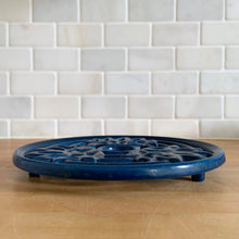 Load image into Gallery viewer, Vintage navy blue round shaped cast iron trivet with lotus flowers. Made in Taiwan, 1970s. Use to safeguard your countertop and tables from hot pots and dishes, or use as wall decor. A charming and practical addition to any kitchen!

In excellent condition.

Measures 8 3/4 x 7/8 inches
