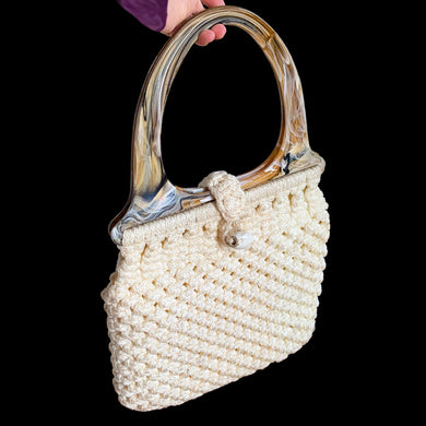 Vintage hand-knotted off-white macrame hand bag features a loop and bead closure, hard plastic handles, and satin lining. A great bohemian 70s style purse to compliment any outfit that may be carried at the elbow or shoulder. A nice sized bag for everyday or a day at the beach.

In vintage condition, needs cleaning.

The bag itself measures 14 x 13 inches and 22 inches with handles