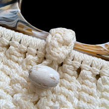 Load image into Gallery viewer, Vintage hand-knotted off-white macrame hand bag features a loop and bead closure, hard plastic handles, and satin lining. A great bohemian 70s style purse to compliment any outfit that may be carried at the elbow or shoulder. A nice sized bag for everyday or a day at the beach.

In vintage condition, needs cleaning.

The bag itself measures 14 x 13 inches and 22 inches with handles
