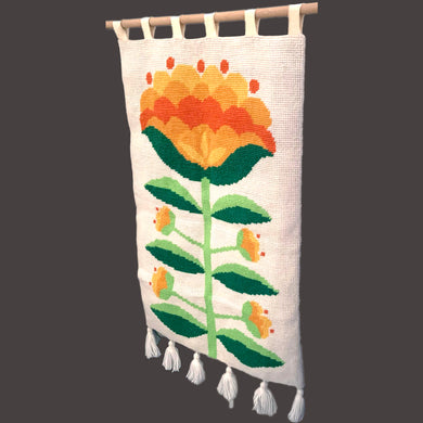 Add a pop of retro charm to your home with our Vintage Handmade Needlepoint Wall Hanging. Featuring a vibrant design of yellow, green, and orange florals on a cream background with decorative fringe, this piece is sure to catch the eye. With hanging double loop felt tabs for easy installation, bring a touch of nostalgia to any room!  In excellent condition, backed with cotton fabric.  Measures 24 1/2 x 45 1/2 (including tabs and fringe)