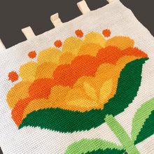 Load image into Gallery viewer, Add a pop of retro charm to your home with our Vintage Handmade Needlepoint Wall Hanging. Featuring a vibrant design of yellow, green, and orange florals on a cream background with decorative fringe, this piece is sure to catch the eye. With hanging double loop felt tabs for easy installation, bring a touch of nostalgia to any room!  In excellent condition, backed with cotton fabric.  Measures 24 1/2 x 45 1/2 (including tabs and fringe)
