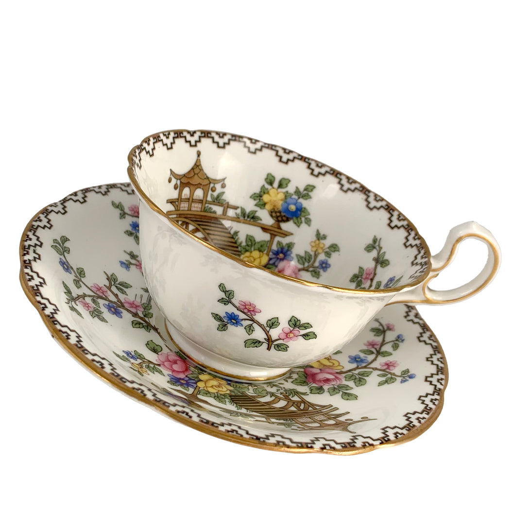 Vintage Pagoda Chinoiserie motif fine bone china teacup and saucer featuring hand painted brown pagoda and flowers in shades of pink, blue, yellow and green with gold gilt trim and scalloped edges. Crafted by Aynsley, England, 1920s. A lovely way to enjoy a cuppa tea!

In excellent condition, no chips, cracks or repairs. Maker's mark on the bottom.

Measures 3 1/2 x 2 1/4 inches | Saucer measures 5 1/2 inches