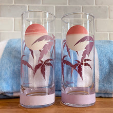 Load image into Gallery viewer, The tropical graphics are the standout feature of these vintage mid-century Panache highball glass tumblers decorated with purple palm trees against a beautiful sunset. Designed by Wolly Clark, circa 1950s. These glasses will definitely add some sweet beachy vibes to your cocktails!  These glasses are free from chips/cracks with minor dishwasher damage  Measures 2 1/2 x 6 1/2 inches  Capacity 13 1/2 ounces
