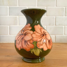 Load image into Gallery viewer, Vintage art pottery vase featuring tubelined hibiscus flowers hand painted in shades of peach on an avocado green ground. Design by Walter Moorcroft. Crafted by Moorcroft Pottery, England, 1980s. A beautiful piece for your art pottery collection or to give as a gift!  In excellent condition, no chips/cracks/repairs. Bottom has impressed marks, &quot;MOORCROFT POTTERY&quot; AND &quot;MADE IN ENGLAND&quot; and gold oval MOORCROFT, England sticker.  Measures 3 3/4 x 5 1/4 inches
