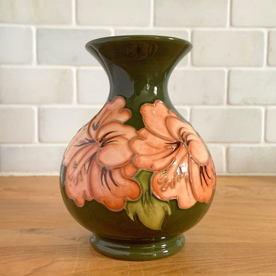 Vintage art pottery vase featuring tubelined hibiscus flowers hand painted in shades of peach on an avocado green ground. Design by Walter Moorcroft. Crafted by Moorcroft Pottery, England, 1980s. A beautiful piece for your art pottery collection or to give as a gift!  In excellent condition, no chips/cracks/repairs. Bottom has impressed marks, 