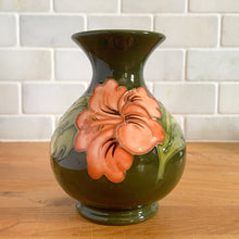 Load image into Gallery viewer, Vintage art pottery vase featuring tubelined hibiscus flowers hand painted in shades of peach on an avocado green ground. Design by Walter Moorcroft. Crafted by Moorcroft Pottery, England, 1980s. A beautiful piece for your art pottery collection or to give as a gift!  In excellent condition, no chips/cracks/repairs. Bottom has impressed marks, &quot;MOORCROFT POTTERY&quot; AND &quot;MADE IN ENGLAND&quot; and gold oval MOORCROFT, England sticker.  Measures 3 3/4 x 5 1/4 inches
