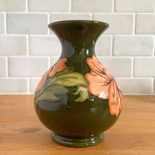 Load image into Gallery viewer, Vintage art pottery vase featuring tubelined hibiscus flowers hand painted in shades of peach on an avocado green ground. Design by Walter Moorcroft. Crafted by Moorcroft Pottery, England, 1980s. A beautiful piece for your art pottery collection or to give as a gift!  In excellent condition, no chips/cracks/repairs. Bottom has impressed marks, &quot;MOORCROFT POTTERY&quot; AND &quot;MADE IN ENGLAND&quot; and gold oval MOORCROFT, England sticker.  Measures 3 3/4 x 5 1/4 inches
