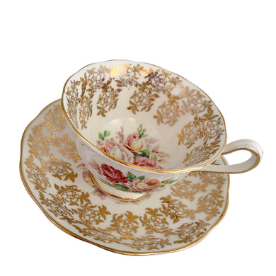 Traditional vintage mid-century era Avon shaped teacup and saucer featuring hand painted pink cabbage roses and heavy gold filigree pattern of flowers on the cup and saucer interiors with gently scalloped gold gilt rims. Crafted by Royal Albert, England, circa 1950s. A beautiful gift or addition to your collection!