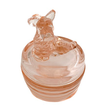 Load image into Gallery viewer, Vintage Jeannette Glass pink depression glass powder jar with lid, angled front view from slightly above, showing the seated terrier dog finial with textured fur and upright tail, flat domed lid with concentric ring detail, ribbed rounded base in blush pink glass
