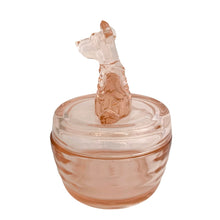 Load image into Gallery viewer, Vintage Jeannette Glass pink depression glass powder jar with lid, left side profile view, showing the seated terrier dog finial in profile with long neck, pointed ears, and textured fur body, flat domed lid with concentric ring detail, ribbed rounded base in blush pink glass
