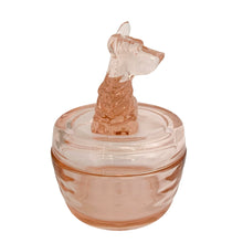 Load image into Gallery viewer, Vintage Jeannette Glass pink depression glass powder jar with lid, right side profile view, showing the seated terrier dog finial in profile with pointed ears, textured fur detail on body, flat domed lid with concentric ring detail, ribbed rounded base in blush pink glass
