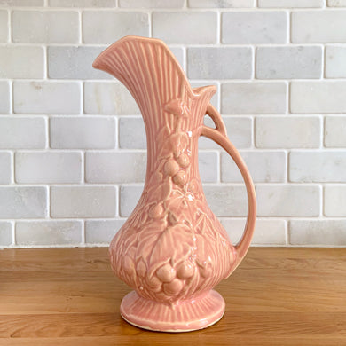 Beautiful vintage Art Deco pink pitcher vase features a unique handle and embossed grapevines. Crafted by McCoy Pottery, 1946. This vase is must for any art pottery collector. A lovely way to enhance your home's decor or to give as a gift!

In excellent vintage condition, no chips/cracks/repairs. Typical manufacturer's glaze misses/pops. Maker's mark on the bottom.

Measures 5 x 9 1/4 inches (incl. handle/spout)