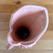 Load image into Gallery viewer, Beautiful vintage Art Deco pink pitcher vase features a unique handle and embossed grapevines. Crafted by McCoy Pottery, 1946. This vase is must for any art pottery collector. A lovely way to enhance your home&#39;s decor or to give as a gift!

In excellent vintage condition, no chips/cracks/repairs. Typical manufacturer&#39;s glaze misses/pops. Maker&#39;s mark on the bottom.

Measures 5 x 9 1/4 inches (incl. handle/spout)
