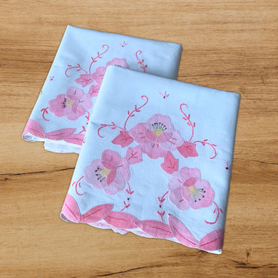 An exquisite pair of vintage white cotton pillowcases, featuring skillfully appliquéd flowers in shades of pink and yellow,  pink and green embroidery, all smartly finished with a scalloped edge of appliquéd leaves. A stunning addition to your bed linens!  In excellent condition. New old stock.  Measures 30 x 19 3/4 inches. 