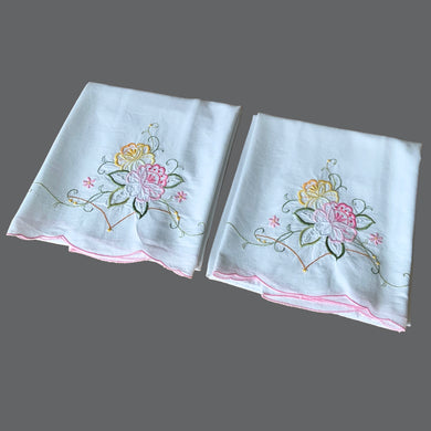 A pair of vintage white cotton pillowcases, featuring elegantly embroidered pink and yellow roses, green leaves with cutwork finished in a sweet pink scalloped edge. A gorgeous addition to your bed linens!

In excellent condition.

Measures 31 1/2 x 19 inches