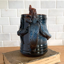 Load image into Gallery viewer, Rare vintage handmade Poseidon and Mermaid redware pottery mug finished in high fired two tone blue glaze on the exterior and a clear glazed interior. This large mug features a figural god of the sea wrapped around the exterior and mermaid in the interior of the mug. Crafted by KD Gandas, Lithuania 1990s. The perfect vessel for your favourite hot beverage!

In excellent condition with original sticker and impressed maker&#39;s mark.

Measures 6 1/4 x 4 1/4 x 6 1/2 inches (incl. handle)

Capacity 16 ounces
